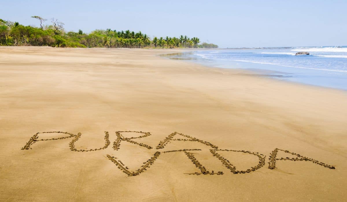 Pura Vida written in the sand of a beach